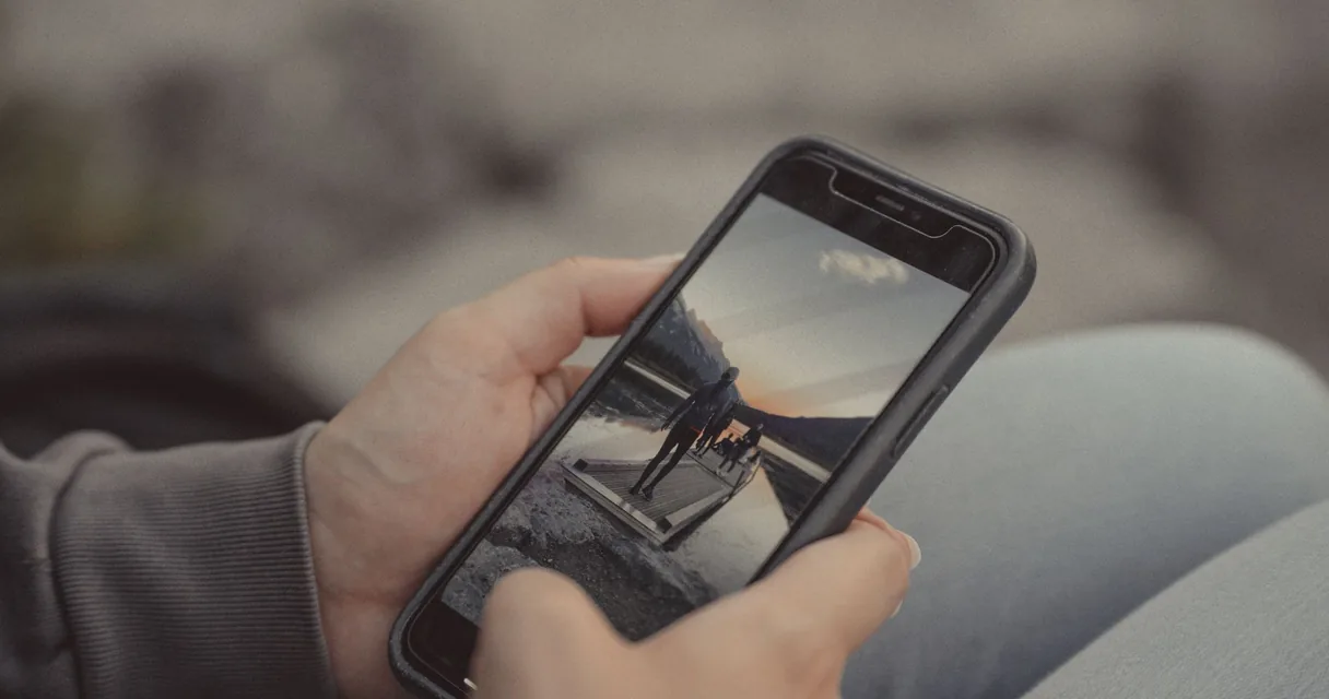 Mão segurando um celular com um vídeo na tela, ilustrando os aplicativos de IPTV no iPhone